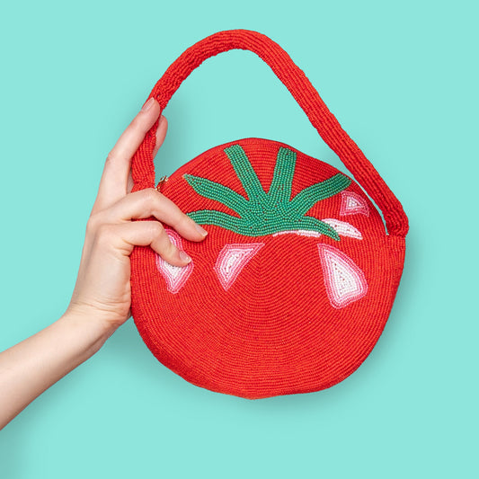 A person holding a red tomato-shaped bag with a green leaf design on the handle.